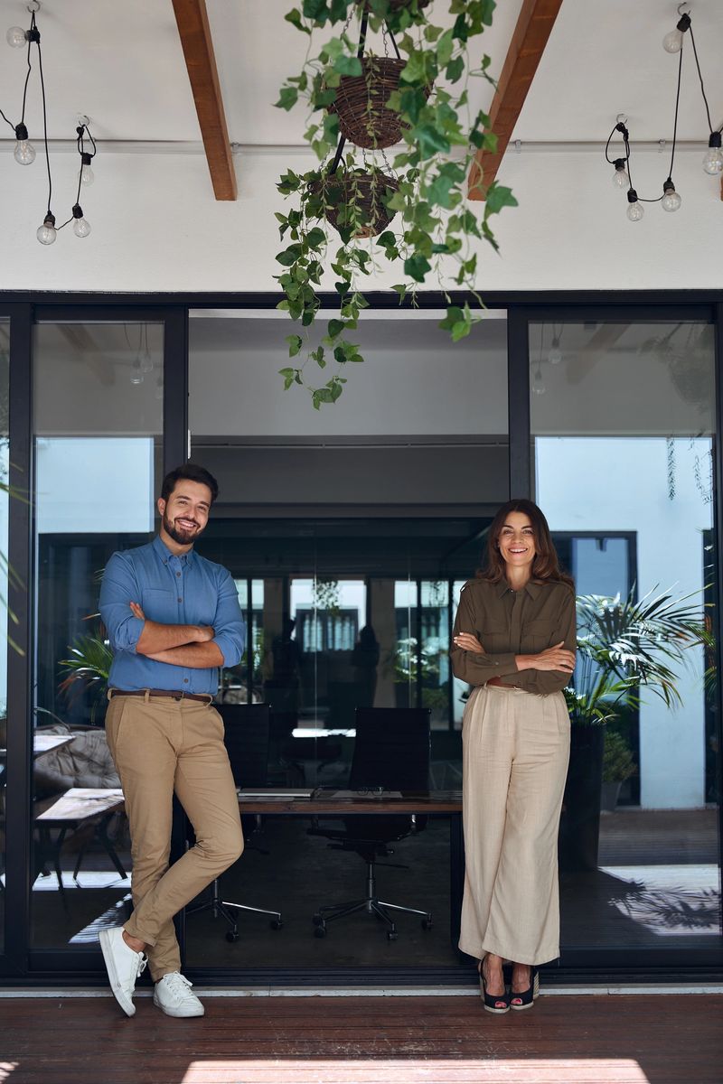Two professional business partners executives standing looking at camera. 2 managers, company managers posing for corporate portrait in modern cozy office, vertical full body photo.