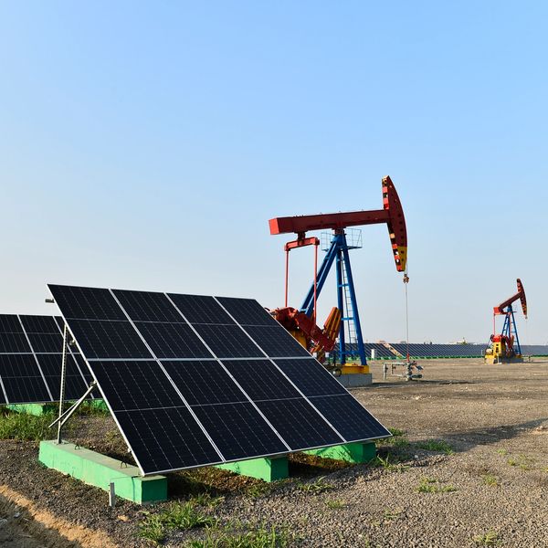 Solar panels and oil pump jacks in a field under clear sky.