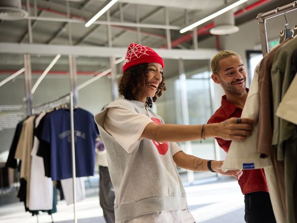 Two people shopping and smiling at clothes on a rack.