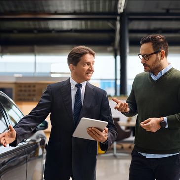 Two men discussing a car in a showroom.