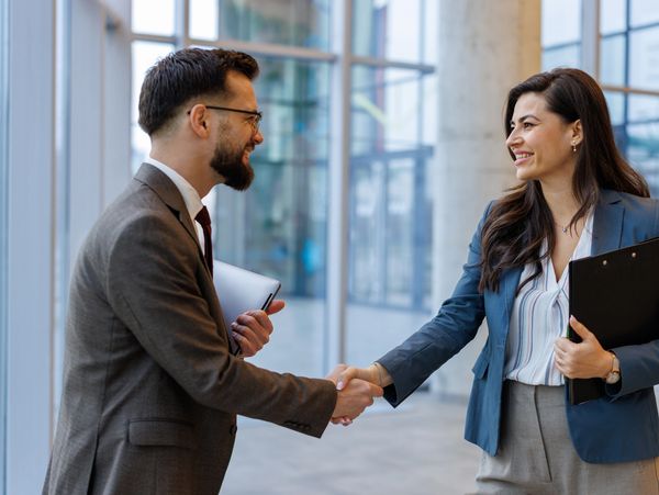 Two professionals shaking hands in a modern office setting.