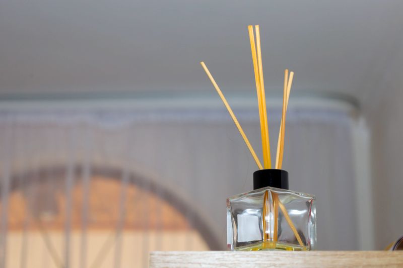 A stylish glass aroma diffuser with wooden sticks stands on a light shelf, creating an atmosphere of peace and coziness in a modern interior. This aesthetic accessory is perfect for home fragrancing, relaxation, aromatherapy,