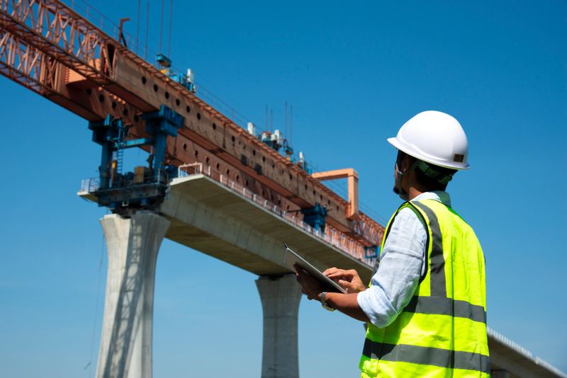 Surveyors and civil engineers using a total station and construction blueprints for railway structure infrastructure."