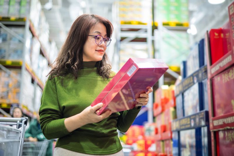 Smiling woman with shopping cart choosing products in supermarket.