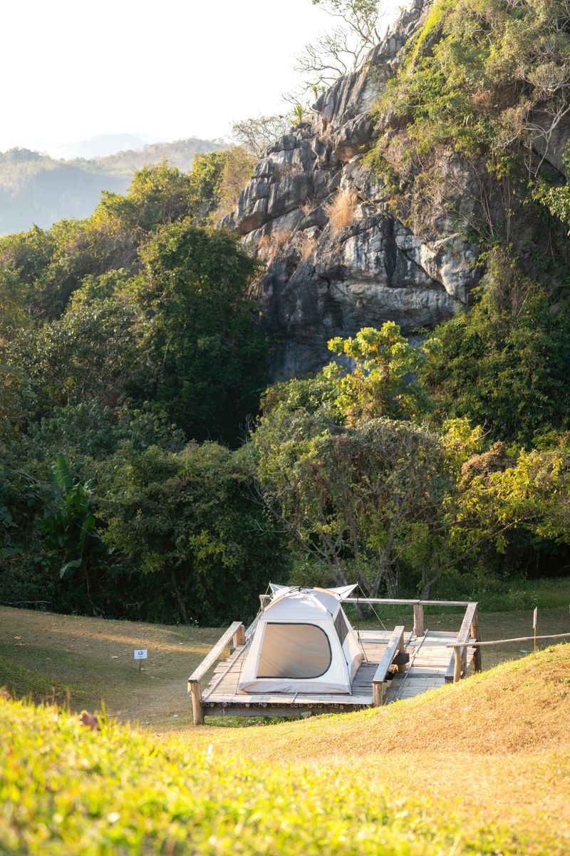 A white camping tent in greenery grass slope and forest environment at natural parkland. Adventure lifestyle and outdoor activity.