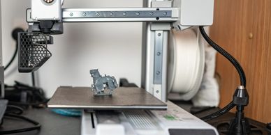 3D printer creating a small gray horse figurine on the print bed.