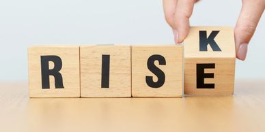 Wooden blocks spelling "RISK" with a hand adjusting the last letter.