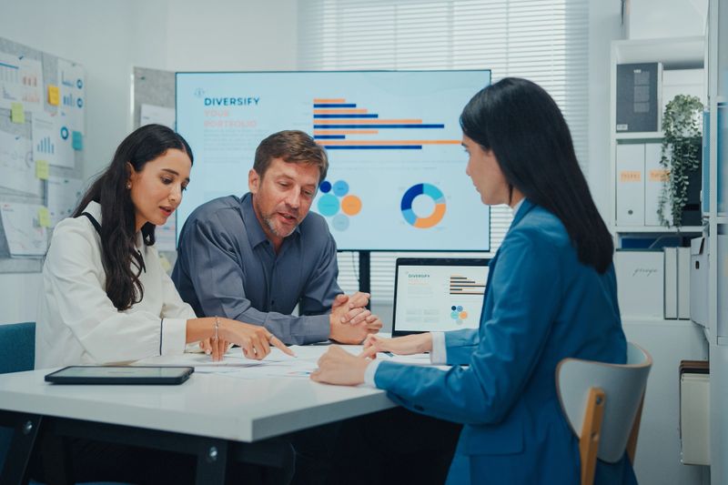 Business team strategy reviews project meeting in modern office. Discussing a workflow diagram on a large screen with a laptop open on table. Teamwork, strategy, and structured collaboration.