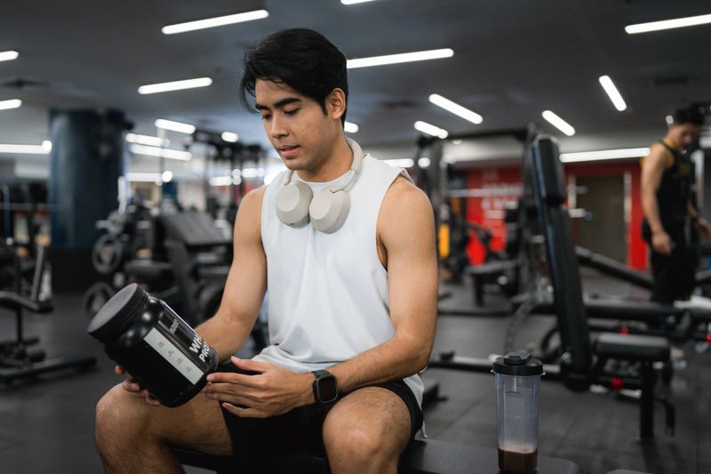 A fit man sits confidently on a bench, drinking a pre-workout whey protein shake to fuel his body with essential nutrients. Focused and energized, he prepares himself for an intense and effective workout session ahead