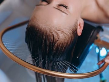 Person washing hair in a shower with a round metal frame.