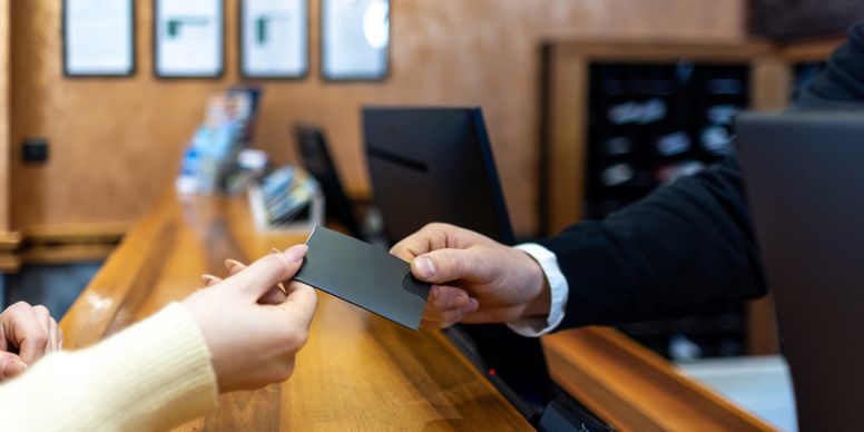 Person handing a black card to a receptionist at a wooden counter