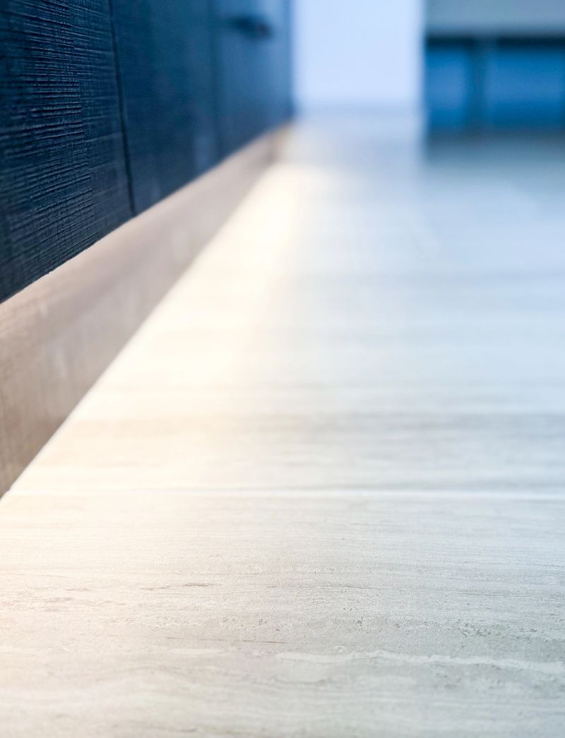 Shallow depth of field interior detail photograph highlighting clean baseboard trim, smooth flooring surface, and textured wall finish inside a newly constructed affordable housing residence, emphasizing craftsmanship, durability, and modern residential construction materials.