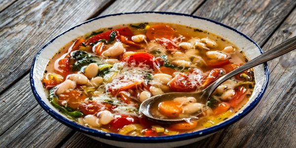 A bowl of vegetable and bean soup with a spoon.