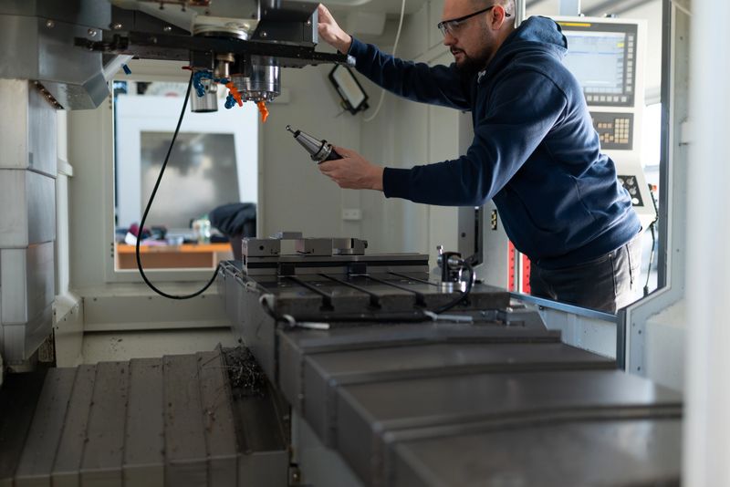 A professional operator installs a tool holder into the spindle of a large-scale CNC milling machine. The image captures the hands-on process of machine setup and industrial maintenance in a high-tech factory environment.