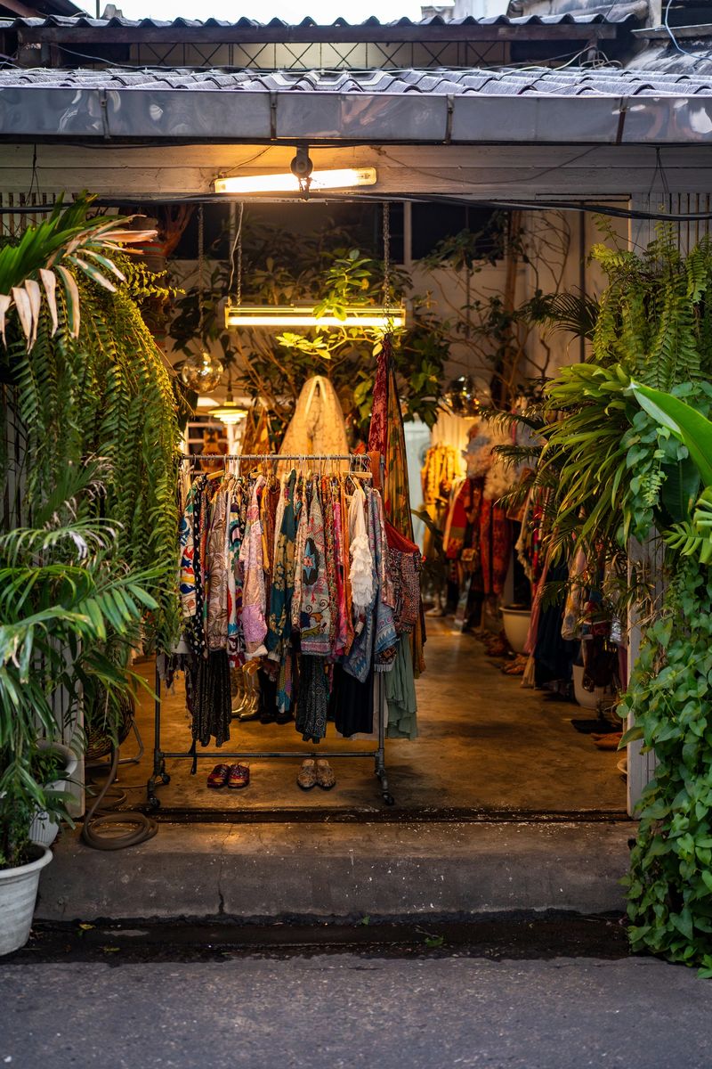 Vintage clothing shop in Asia surrounded by lush tropical plants. Second-hand or thrift store with entrance adorned with vibrant vintage clothes, bohemian style fashion display, sustainable boutique.