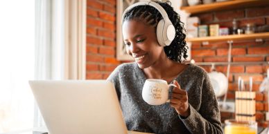 Woman enjoying coffee while working on laptop with headphones.