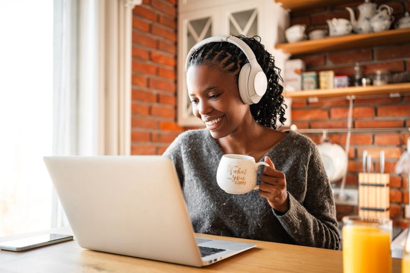 Black woman using laptop and headphone in the kitchen