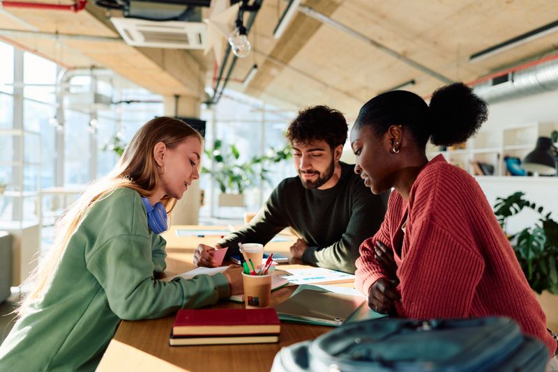 Diverse university students engaging in a group study session, reviewing notes and working together on an academic project at a brightly lit communal table