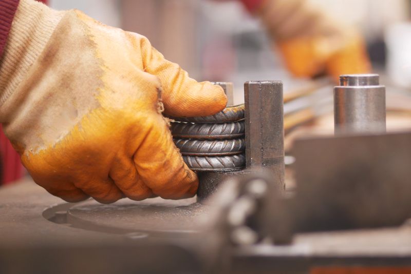 Craftsman uses a tool to bend metal bars in a busy workshop setting.