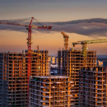 Construction cranes working on high-rise buildings at sunset.