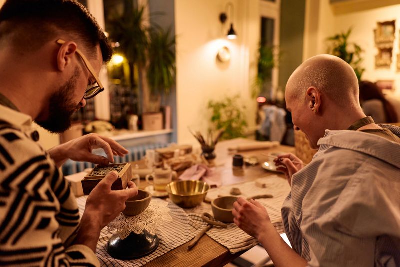 Couple practicing pottery techniques at a shared table, forming and sculpting clay with hands and tools in an intimate ceramics workshop, focused and enjoying the creative process