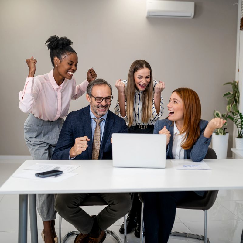 Excited business professionals celebrating a victory or achieving a goal, looking at a laptop in a modern office