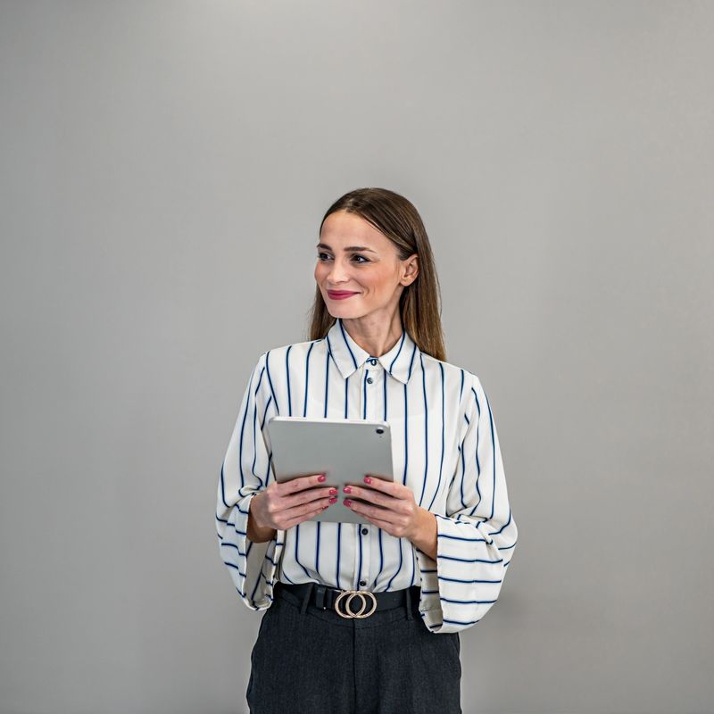 Confident businesswoman holding a digital tablet. She is smiling and looking away, representing innovation and technology in business