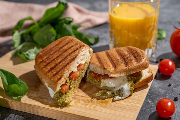 Grilled sandwich with cheese and vegetables on a wooden board.