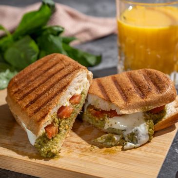 Grilled sandwich with green filling and tomatoes, served with orange juice.