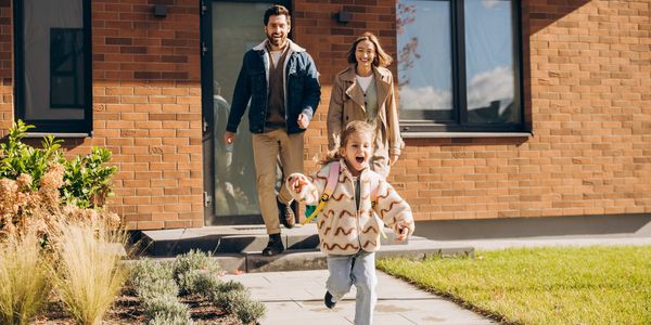 Child runs happily ahead of parents outside a house.