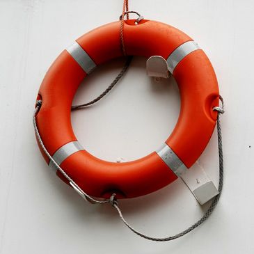 Orange lifebuoy with white reflective strips hanging on a white wall.