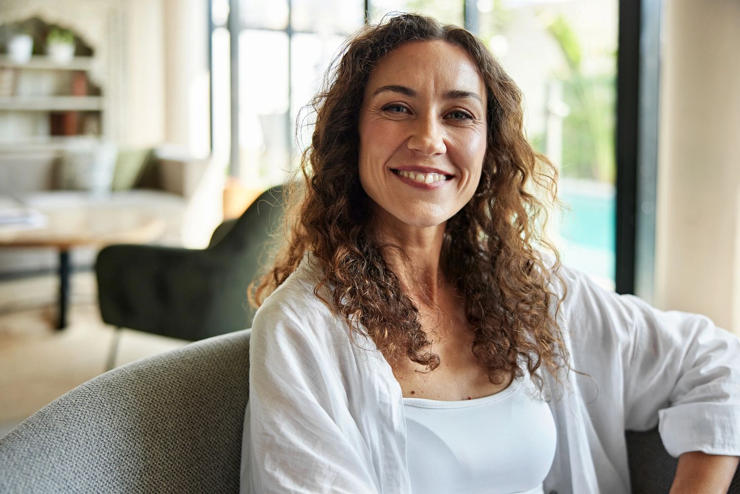 Smiling woman with curly hair sitting indoors.