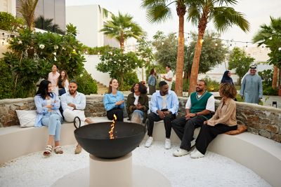 Diverse group of people socializing outdoors around a fire pit.