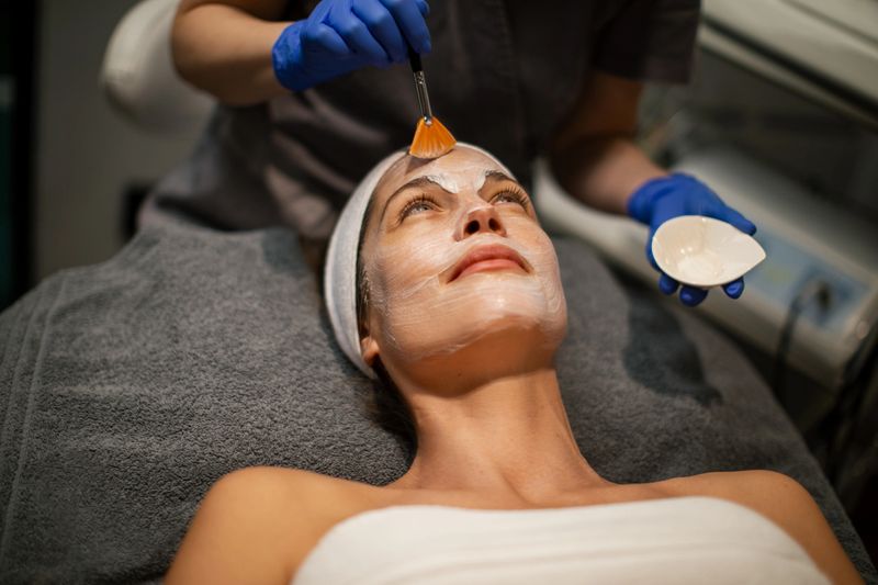 Beautician is applying a facial mask to a woman's face at a modern beauty spa.