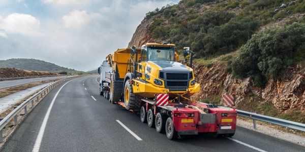 Heavy machinery being transported on a truck on a mountain road.