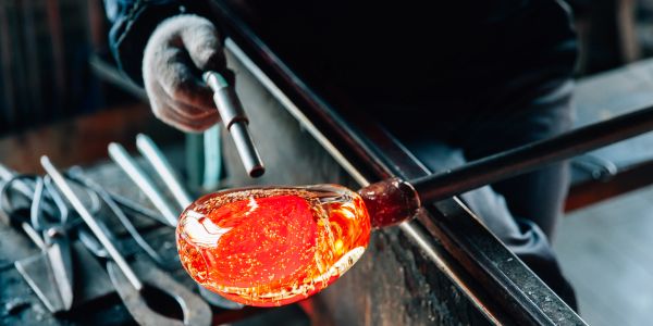 A person shaping molten glass with tools.