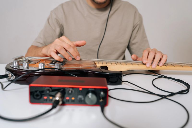 Cropped shot of musician male processing sound from electric bass guitar through audio interface with connected headphones, composing and recording new music at home studio setup.