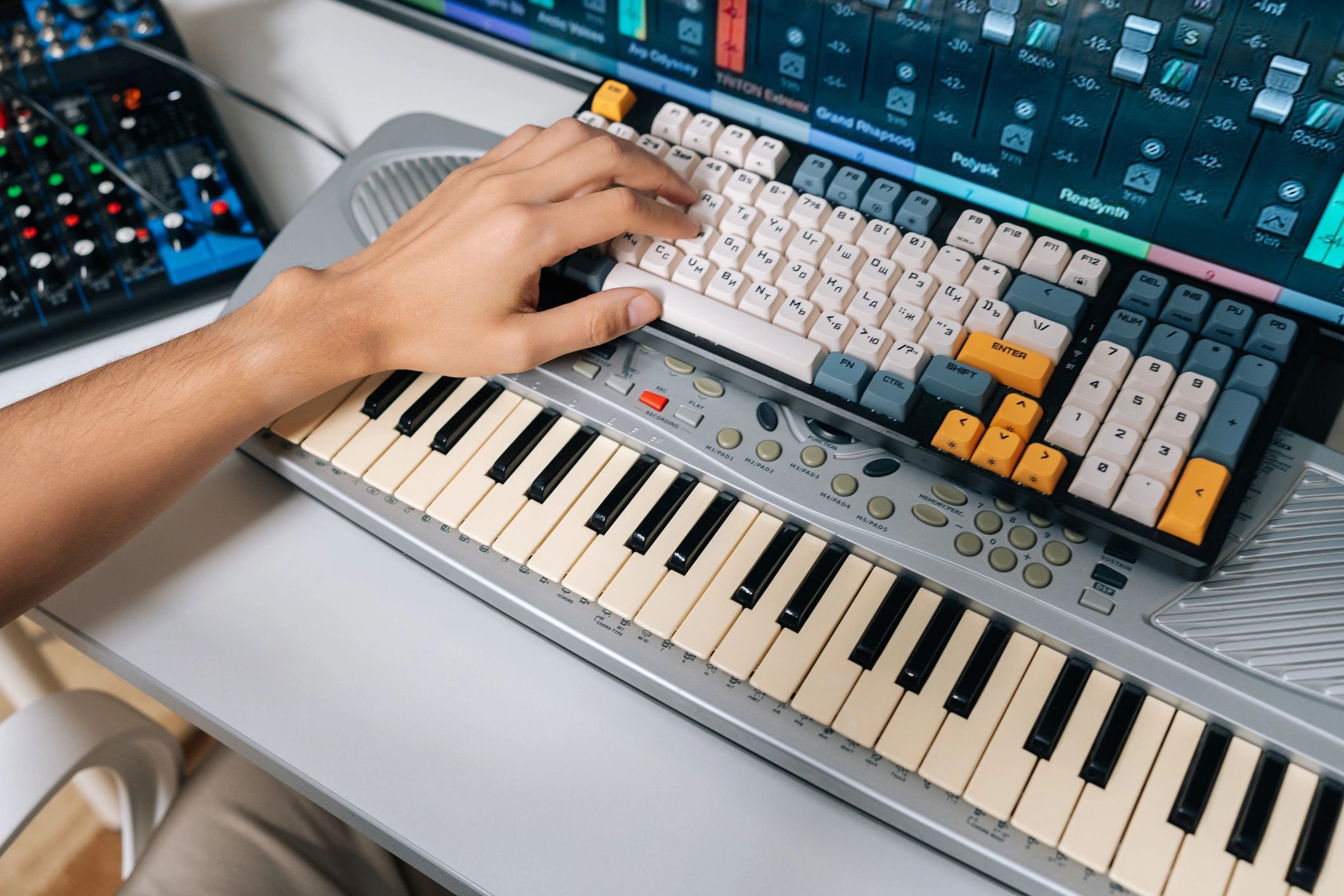 Hand playing a keyboard with a mechanical keyboard on top.