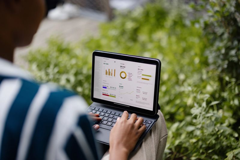 Person typing on a tablet with a keyboard, analyzing financial charts and graphs on the screen outdoors