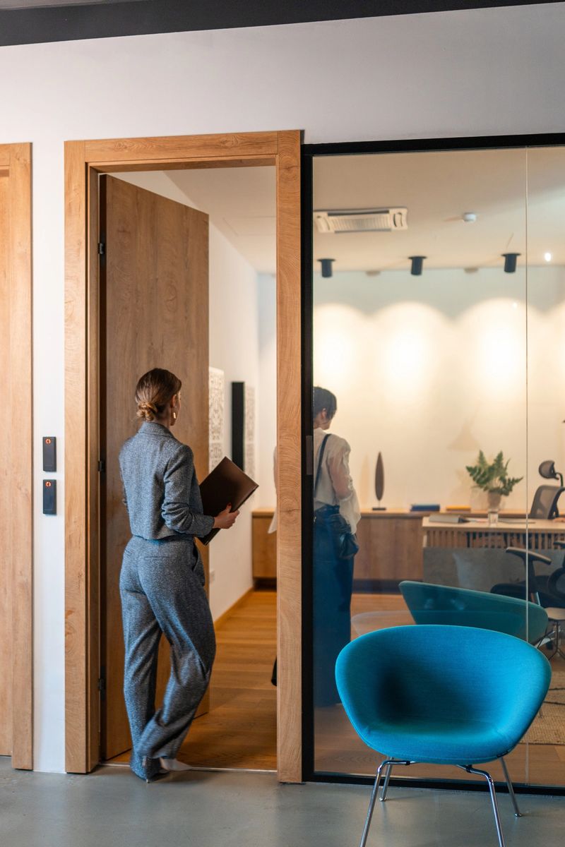 Professional mid-adult Caucasian female human resources manager entering contemporary office space with glass partition and modern furniture design.