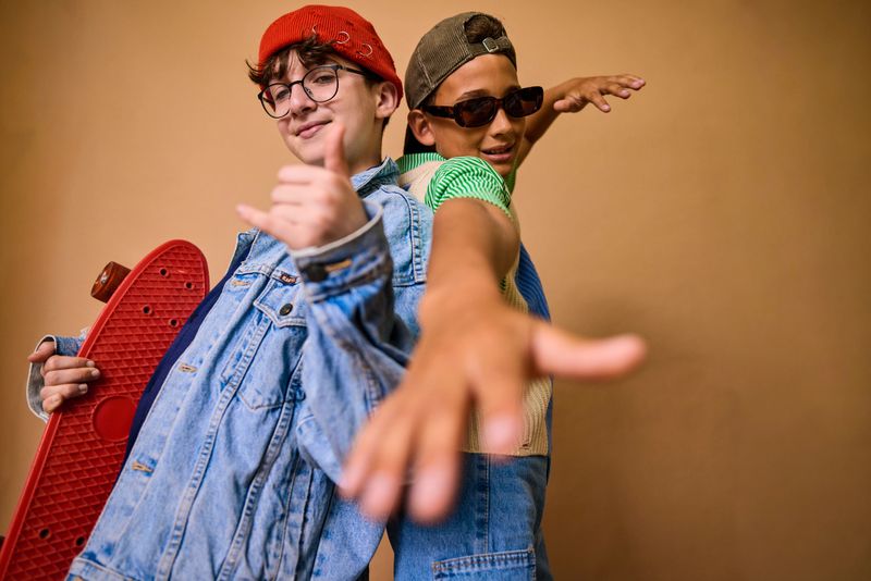 Two young diverse friends posing with a skateboard against a brown background