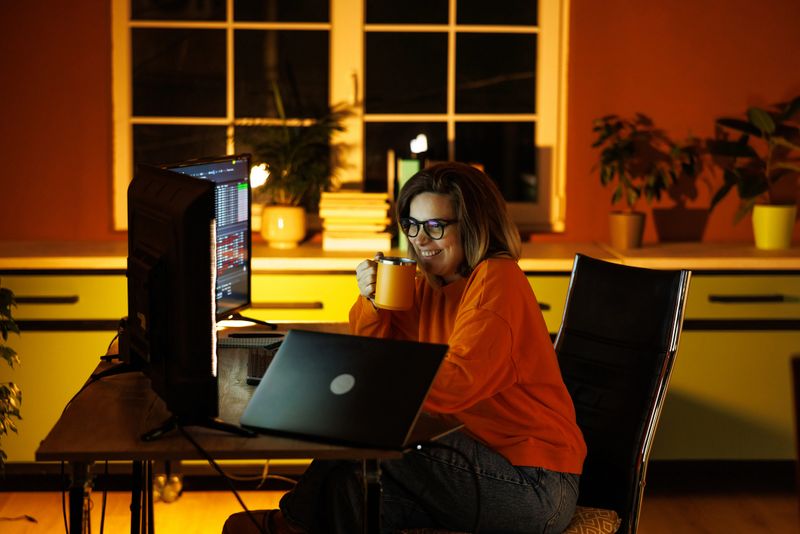 Female computer programmer in her thirties coding on multiple monitors at night in home office