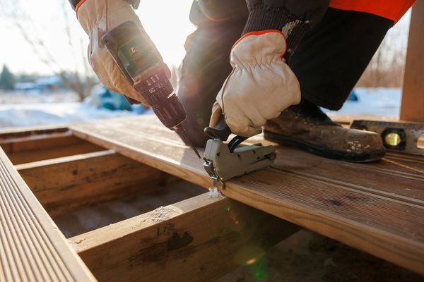 A person using a drill and staple gun on wooden planks outdoors.