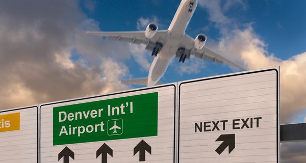 Airplane flying over a highway sign for Denver International Airport.