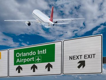 Airplane flying over road signs to Orlando Intl Airport.