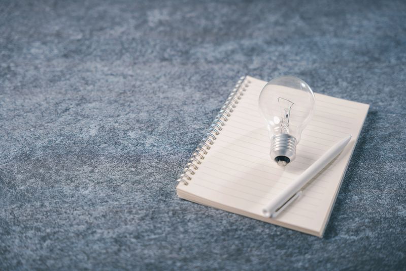 Light bulb on notebook shows knowledge, idea, learning, concept, creative innovation for education or business training, learn from book on dark gray stone textured background.