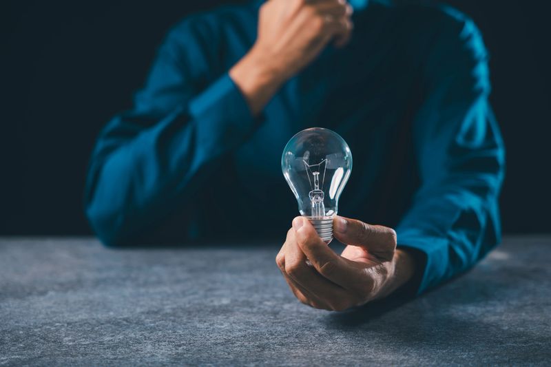 Hand holding lightbulb for idea innovation business concept, inspiration moment shows thinking process with digital power and creative bulb light solutions on dark stone background.