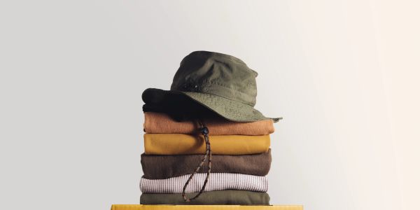 Green hat stacked on folded earthy-toned sweaters against a plain background.