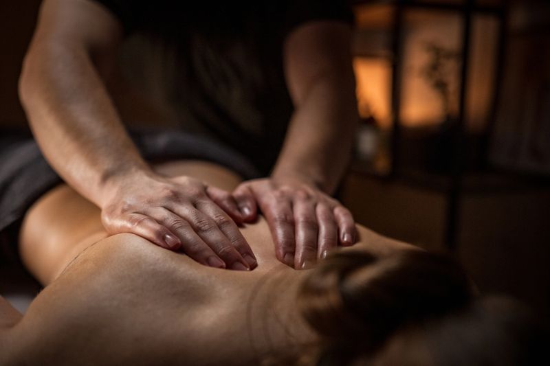A massage therapist's hands gently knead a young woman's back, providing relaxation and relief. The serene setting with warm lighting enhances the calming atmosphere, capturing the essence of alternative therapy and self-care. Professional massage offers soothing benefits.