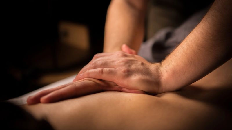 Hands rest on a woman's back, suggesting self-care or relaxation. Soft lighting and a serene expression evoke calm and mindfulness, ideal for alternative therapy, beauty treatments, or massage. Captured with selective focus on detail.